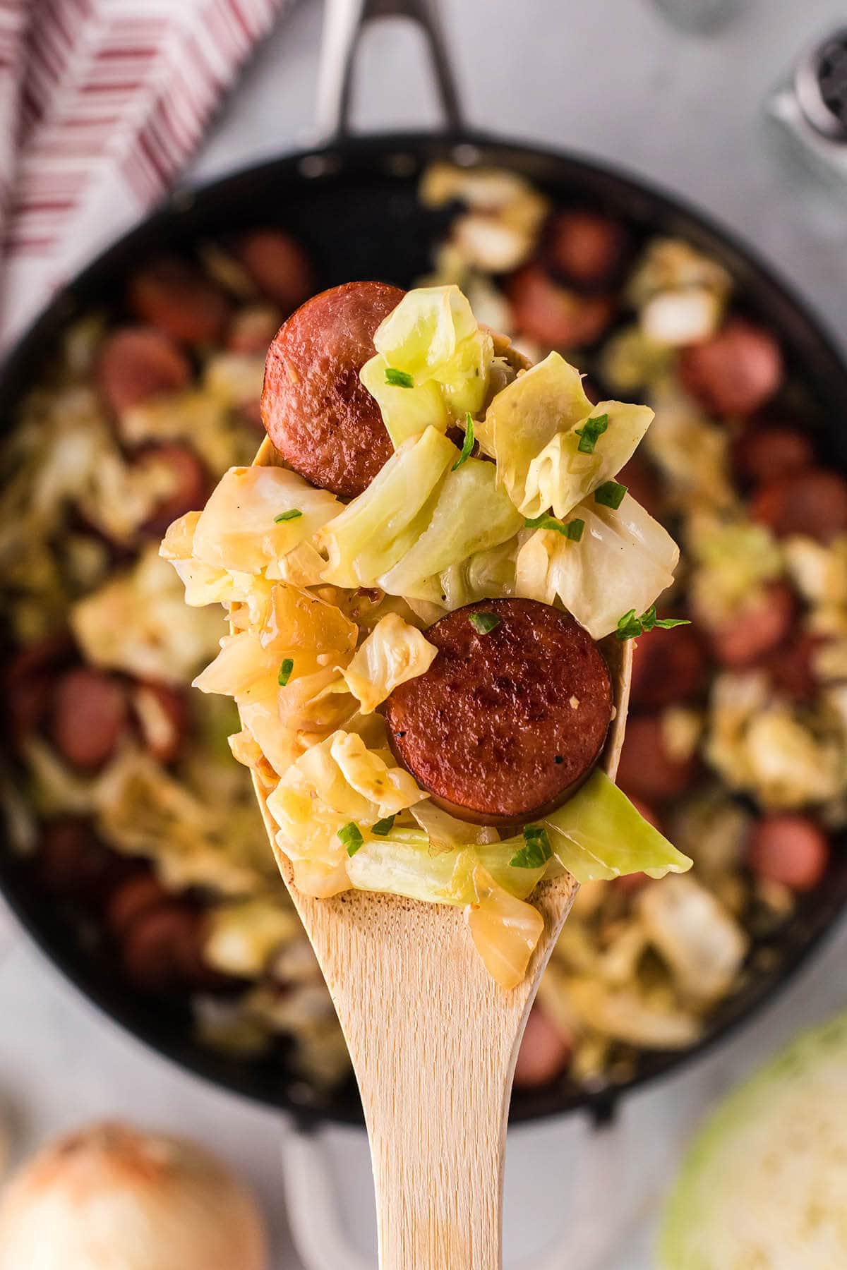 Kielbasa and cabbage in a cast iron with a serving spoon.