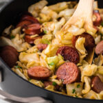 Kielbasa and cabbage in a skillet with a wooden spoon.