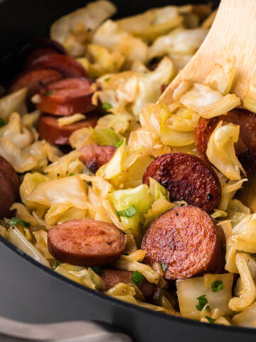 Kielbasa and cabbage in a skillet with a wooden spoon.