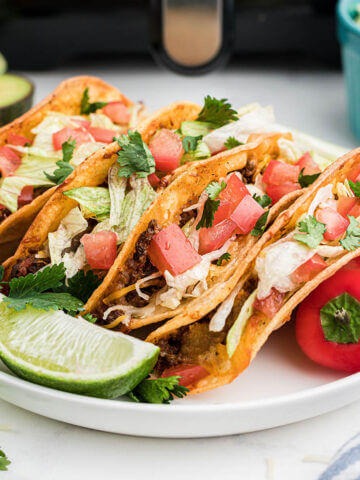 Crispy air fryer tacos on a plate topped with lettuce and chopped tomatoes.