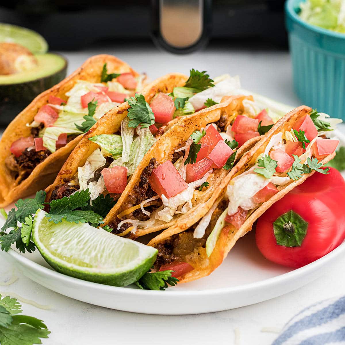 Crispy air fryer tacos on a plate topped with lettuce and chopped tomatoes.