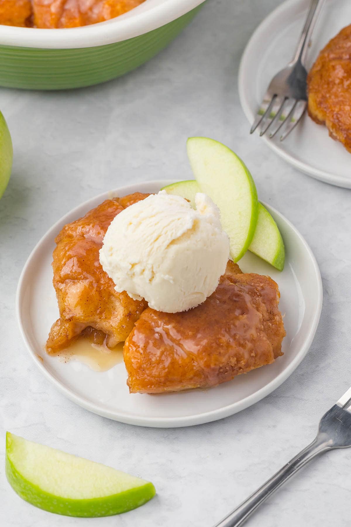 Baked apple dumplings on white plate topped with vanilla ice cream.