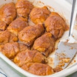 Casserole dish filled with baked apple dumplings, with serving spatula.