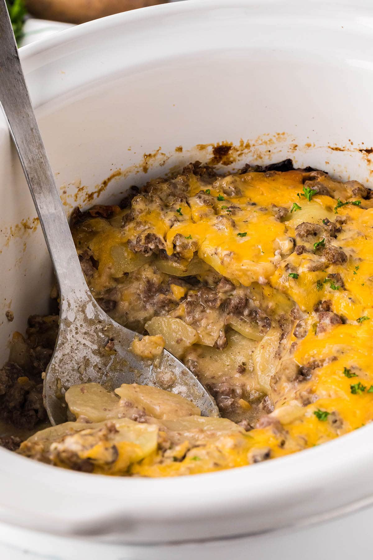 Crockpot Hamburger Potato Casserole in the slow cooker with serving spoon taking out a scoop.