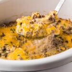 Crockpot Hamburger Potato Casserole in slow cooker with serving spoon scooping out a cheesy serving.
