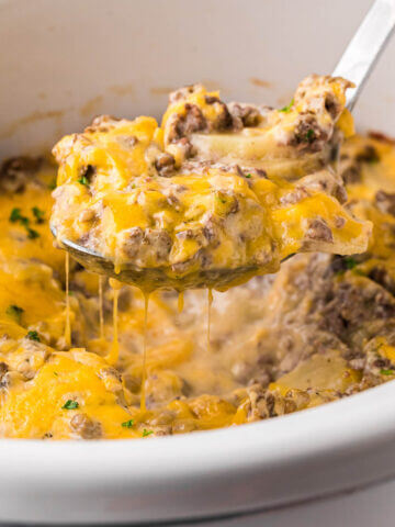 Crockpot Hamburger Potato Casserole in slow cooker with serving spoon scooping out a cheesy serving.