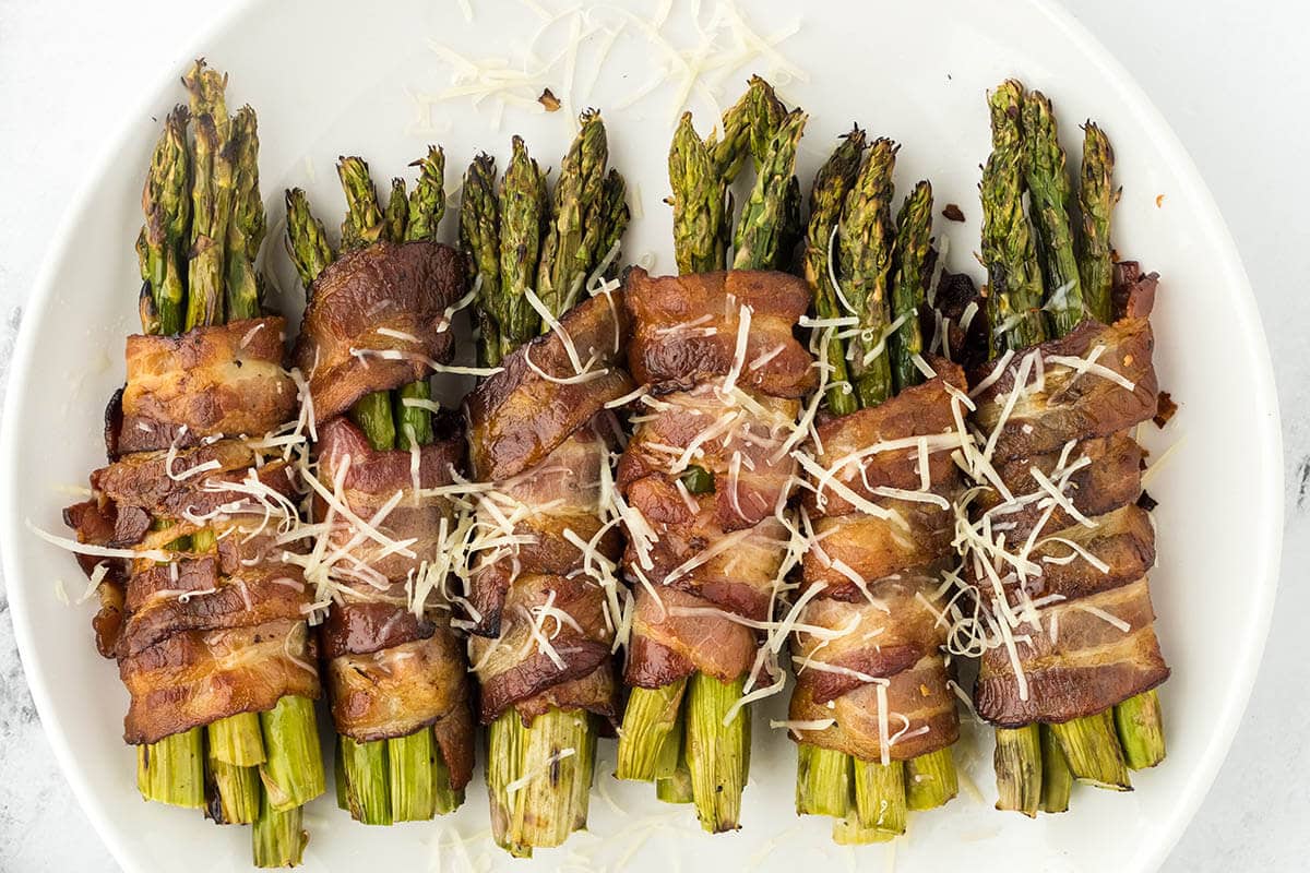 Bacon wrapped asparagus on platter sprinkled with parmesan cheese.