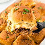 Casserole dish filled with sloppy joe sliders. There's a spatula serving one of the sliders.