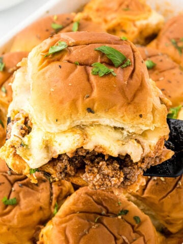 Casserole dish filled with sloppy joe sliders. There's a spatula serving one of the sliders.