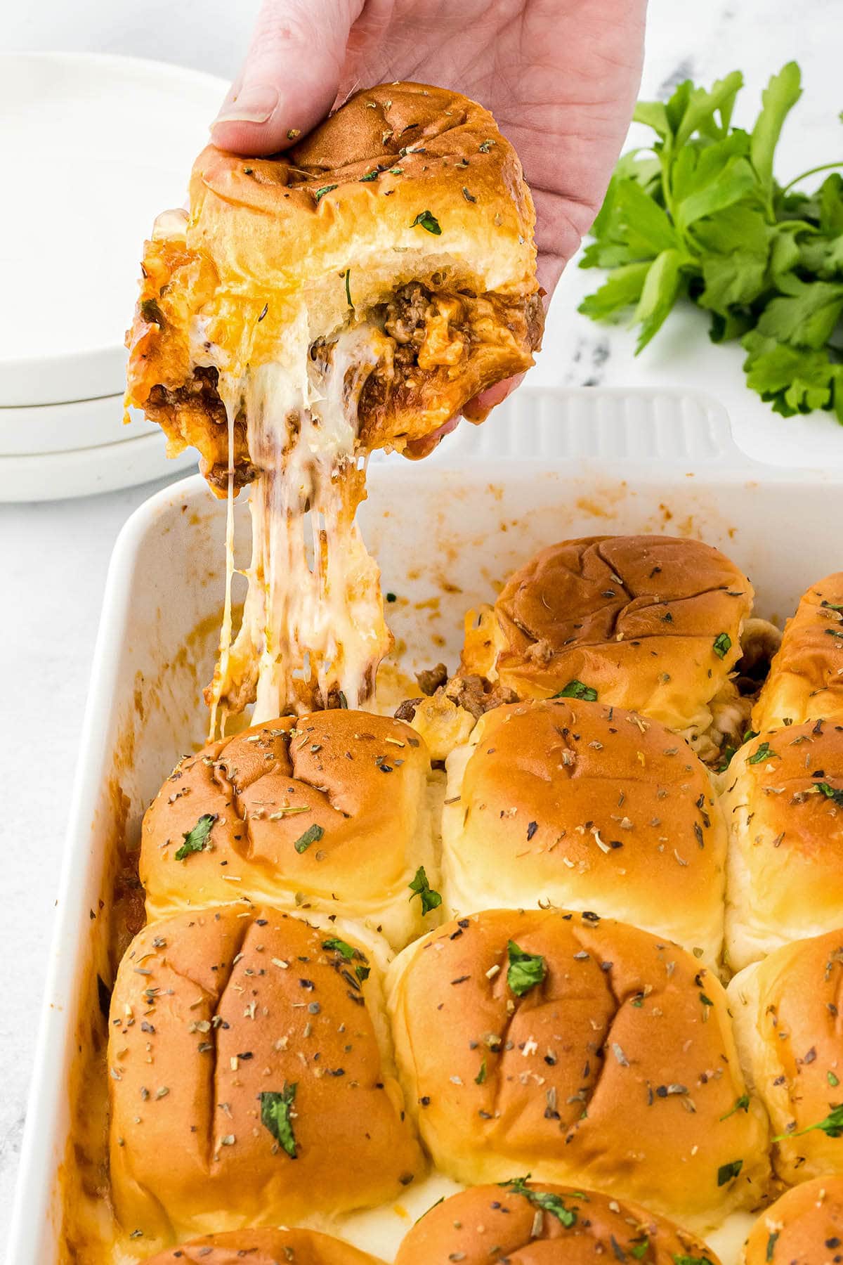 Sloppy Joe sliders in a casserole dish, with one slider being removed from the dish. There's a long cheese stretch.