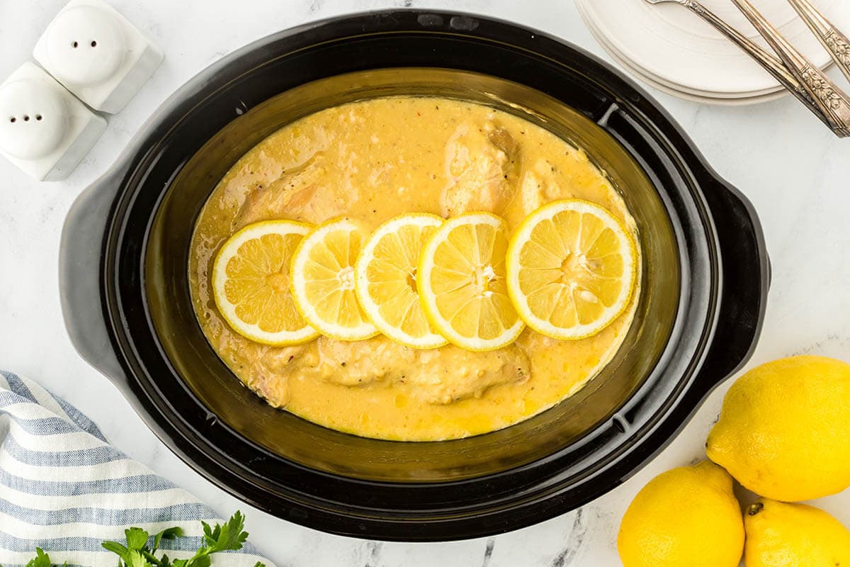 Crockpot Lemon Pepper Chicken in a slow cooker topped with sliced lemon.