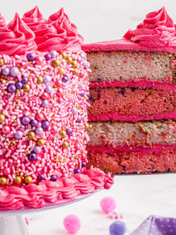 Pink and white funfetti layer cake with a slice being removed from the cake.