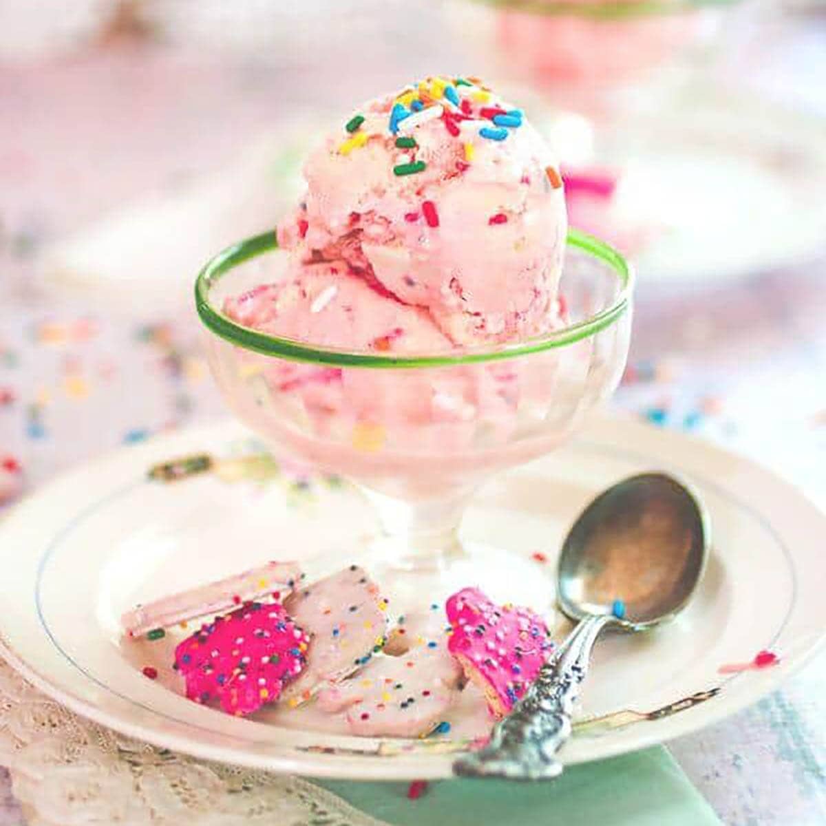 Pink ice cream in a pretty glass bowl with a spoon.