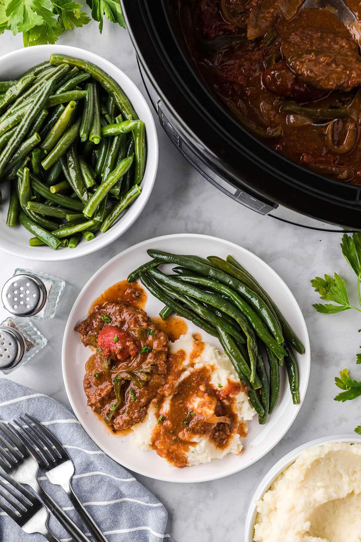 Swiss steak and potatoes topped with gravy and green beans on a plate.