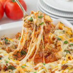 Cheesy pasta in casserole dish, with a serving spoon.