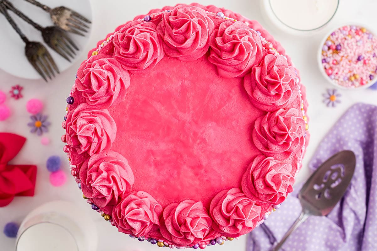 Pretty pink layer cake on table, decorated with pink and purple decorations.