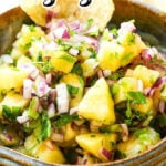 Pineapple Salsa in a bowl, with a chip for dipping. With print overlay for Pinterest.