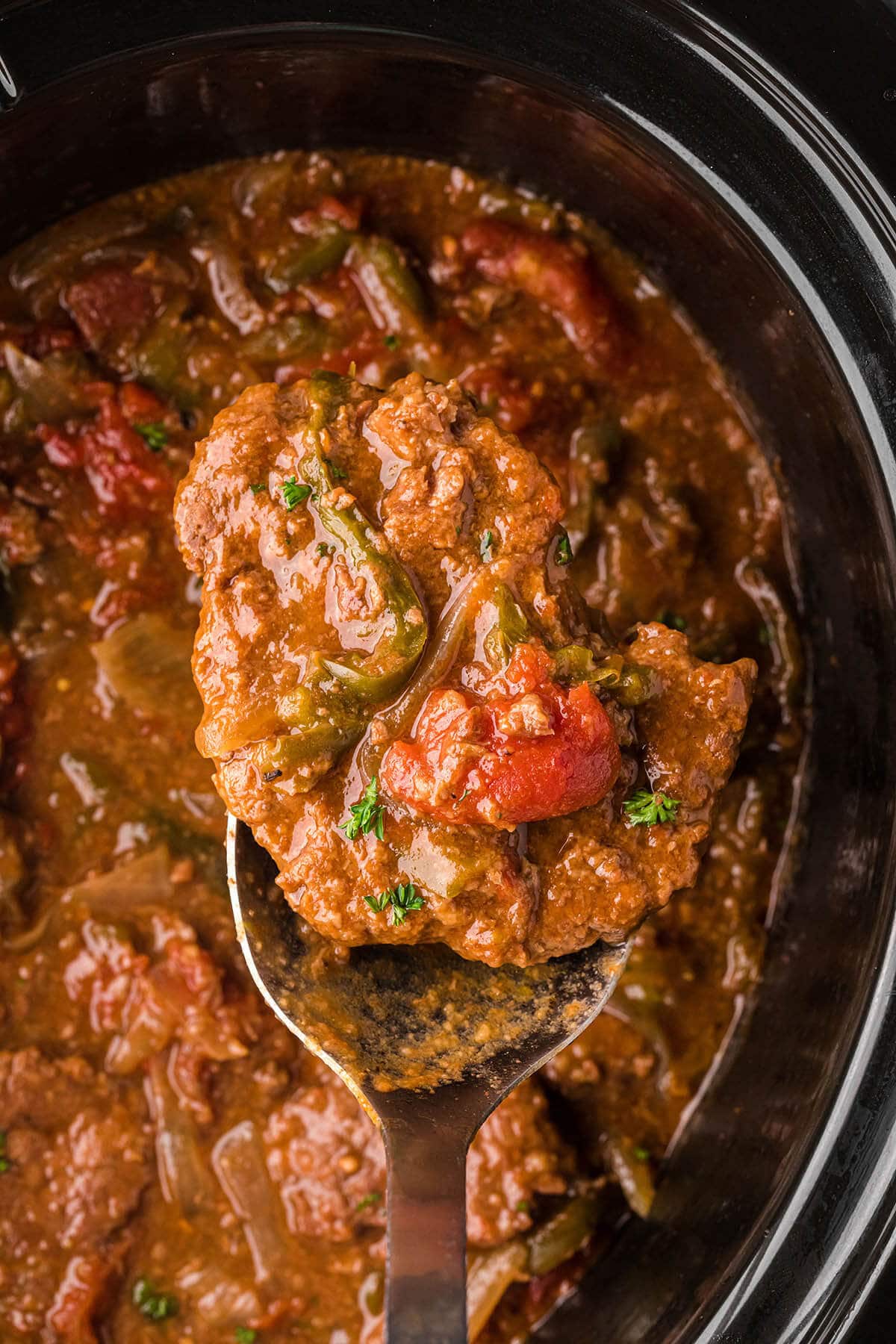 Crockpot Swiss Steak in the slow cooker with spoon scooping out a serving.