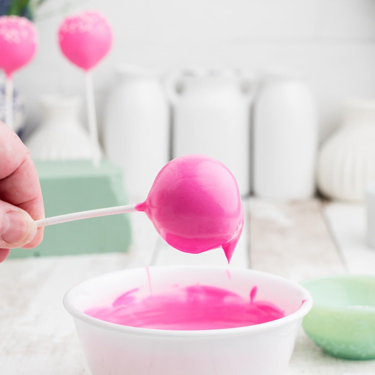 Cake pop being dipped into melted pink chocolate.