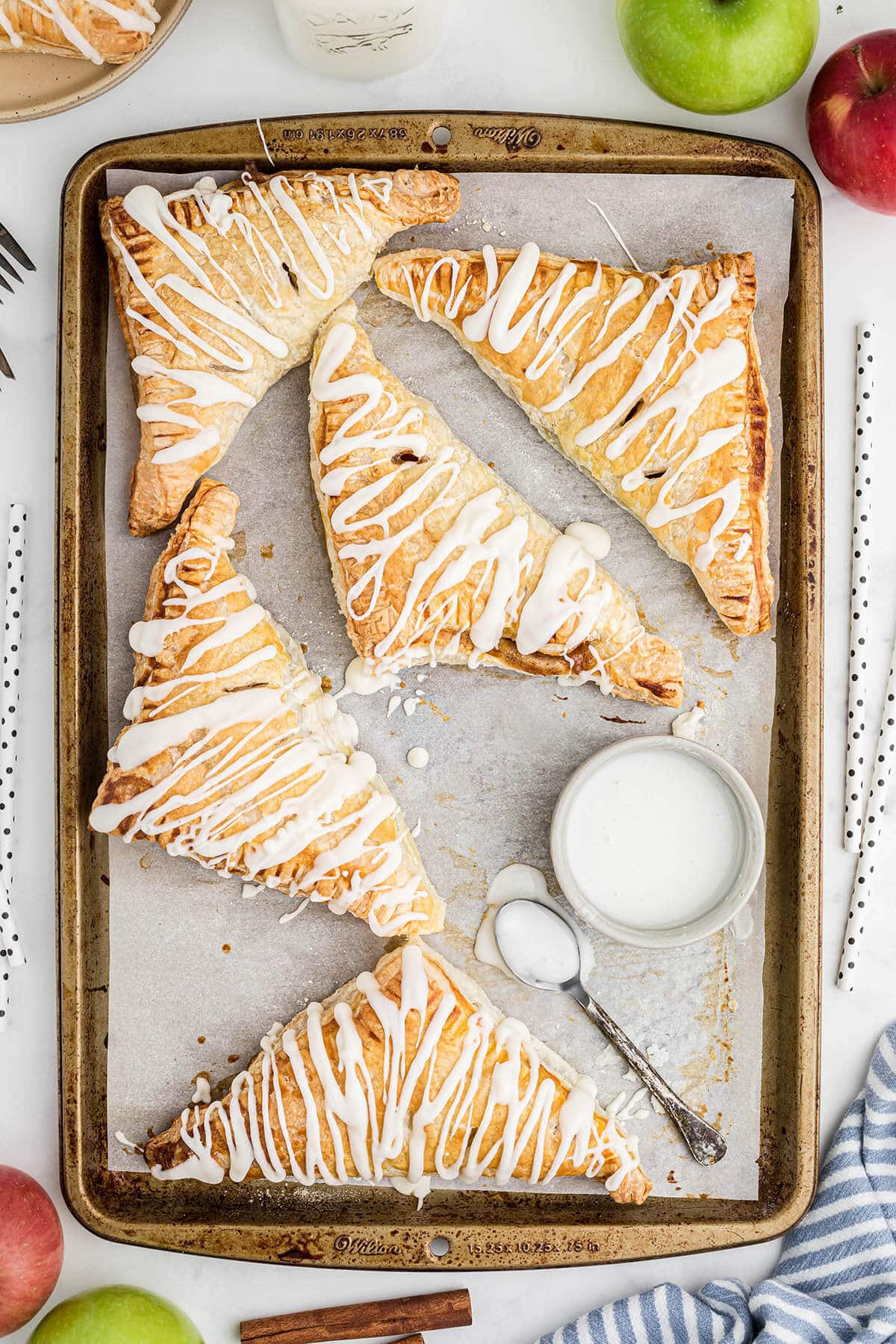 Apple Turnovers on a baking sheet drizzled with icing.