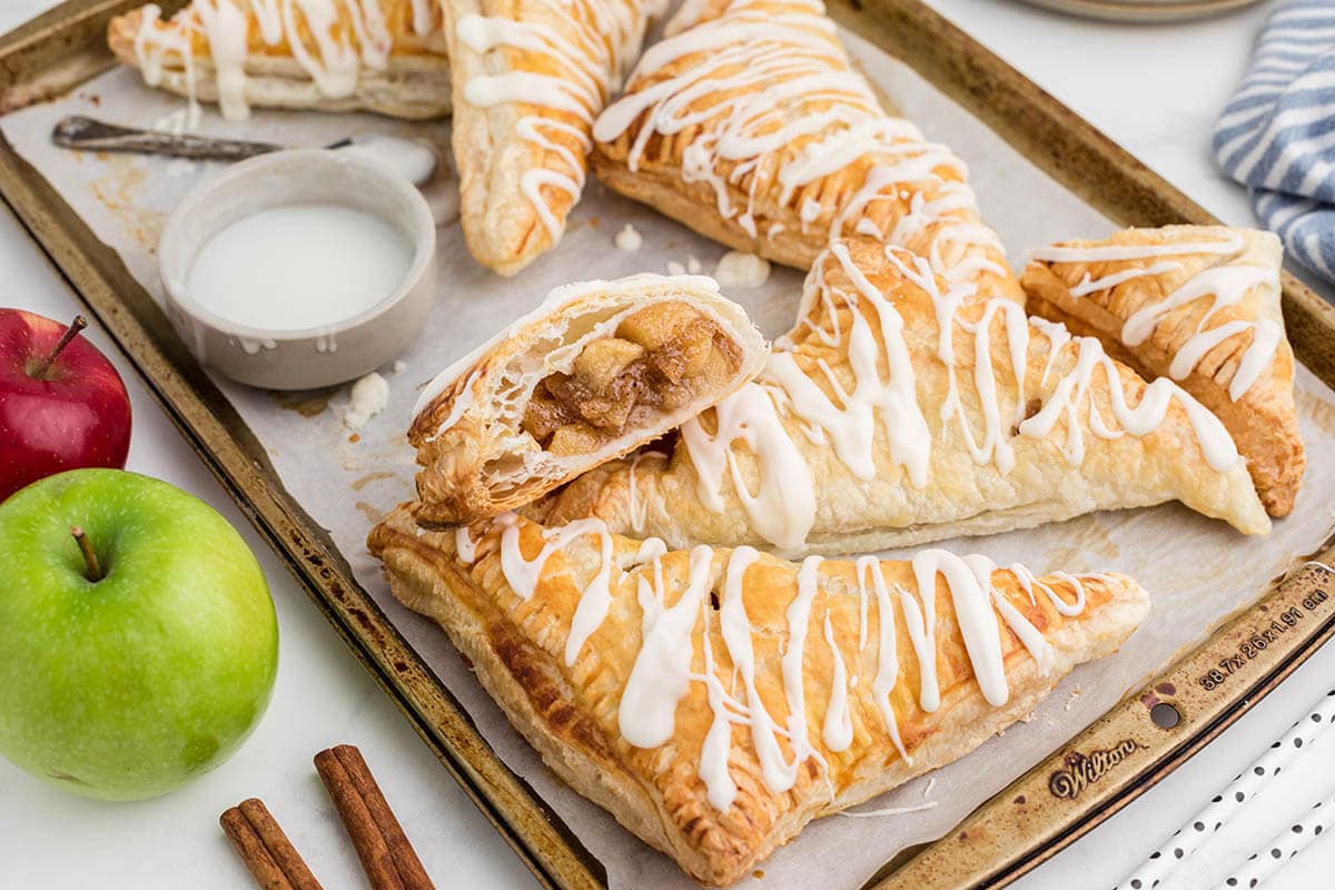 Apple hand pies with puff pastry on a lined baking sheet.