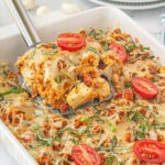 Chicken bruschetta casserole in baking dish with a spatula dishing out a serving.