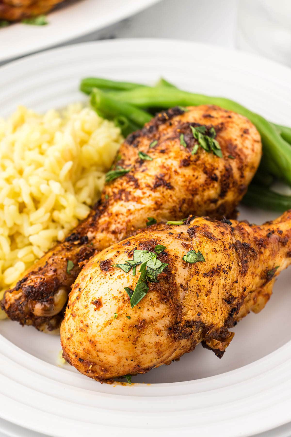 Grilled chicken legs on a plate with rice and steamed green beans.