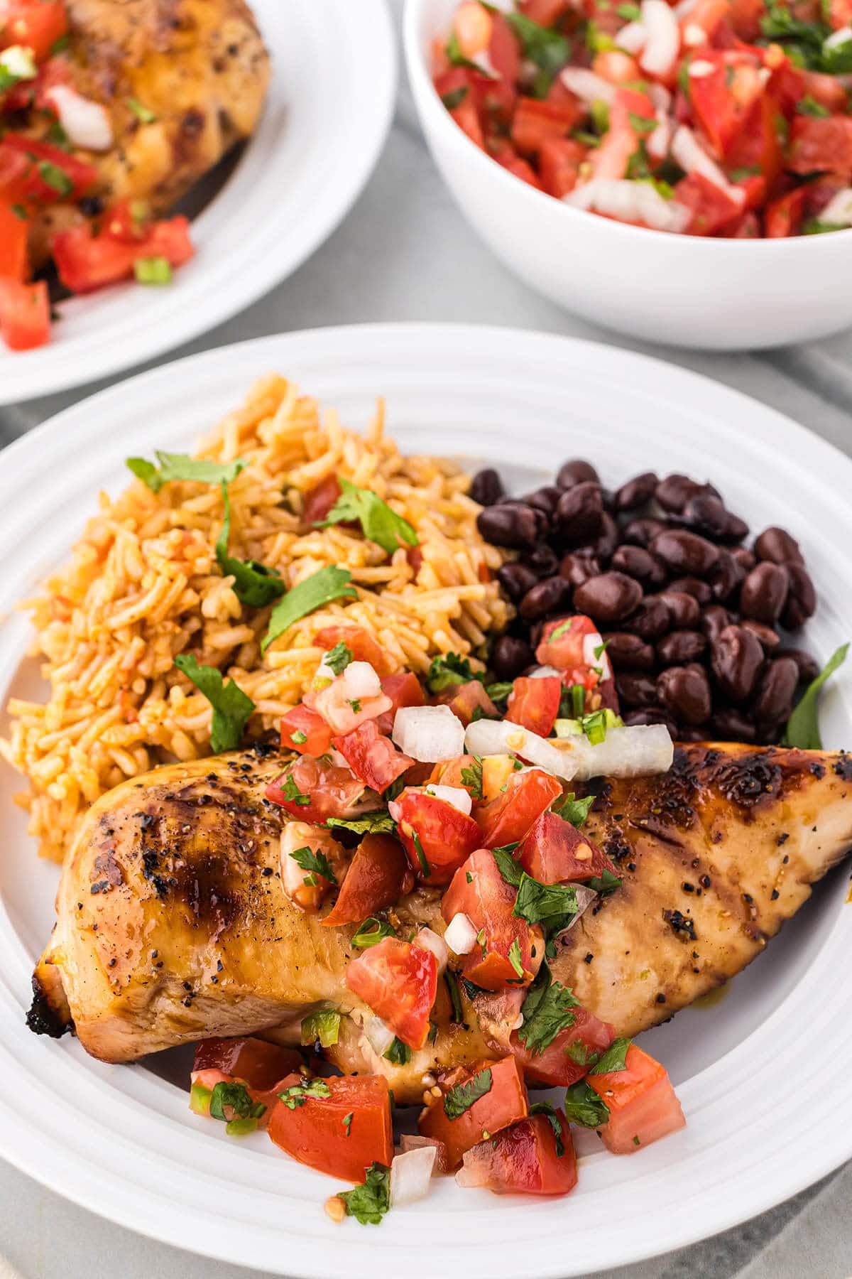 Dinner plate with grilled margarita chicken topped with salsa, black beans and rice.