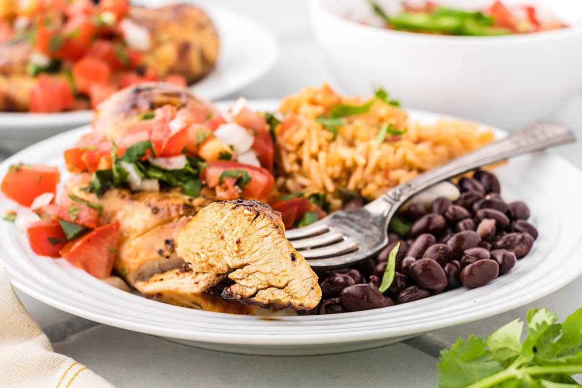 Sliced margarita chicken on plate served with rice and black beans.
