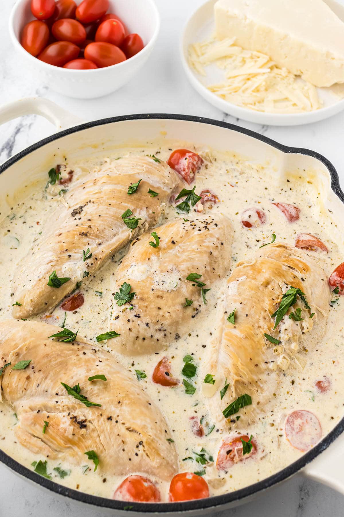 Chicken breast simmering in a creamy white sauce.