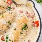 A skillet filled with creamy white sauce with several chicken breasts simmering in the sauce.