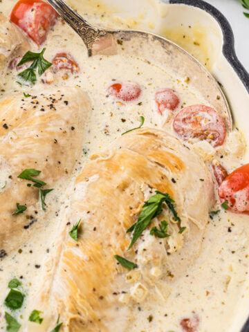 A skillet filled with creamy white sauce with several chicken breasts simmering in the sauce.