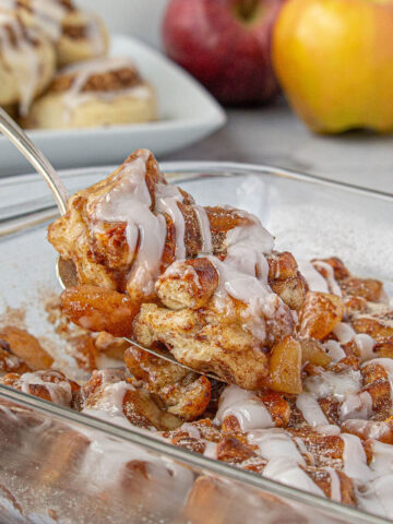 Apple cobbler in a baking dish, with a serving utensil removing a slice.