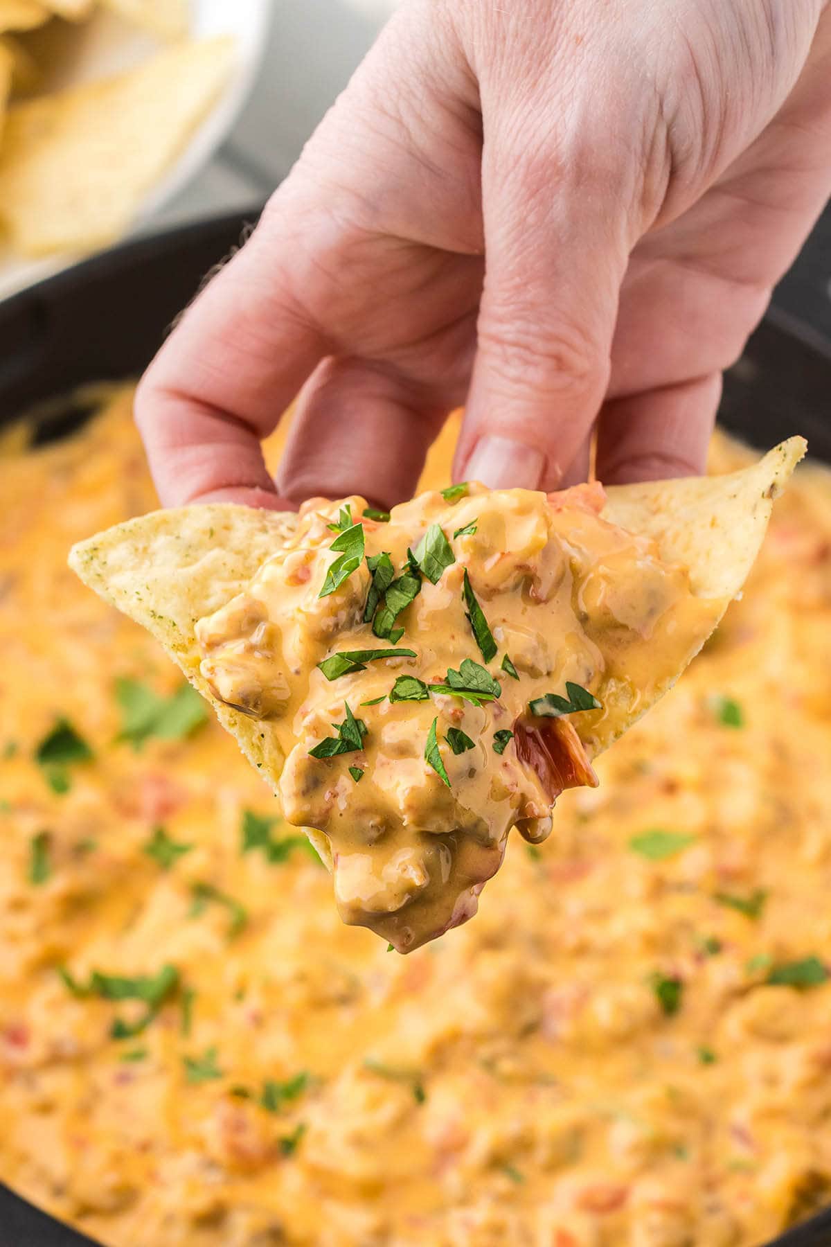 Hand holding tortilla chip filled with sausage and cheese dip, ready to take a bite!