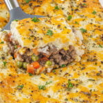 Traditional Cottage Pie in a casserole dish with a spatula scooping out a serving.