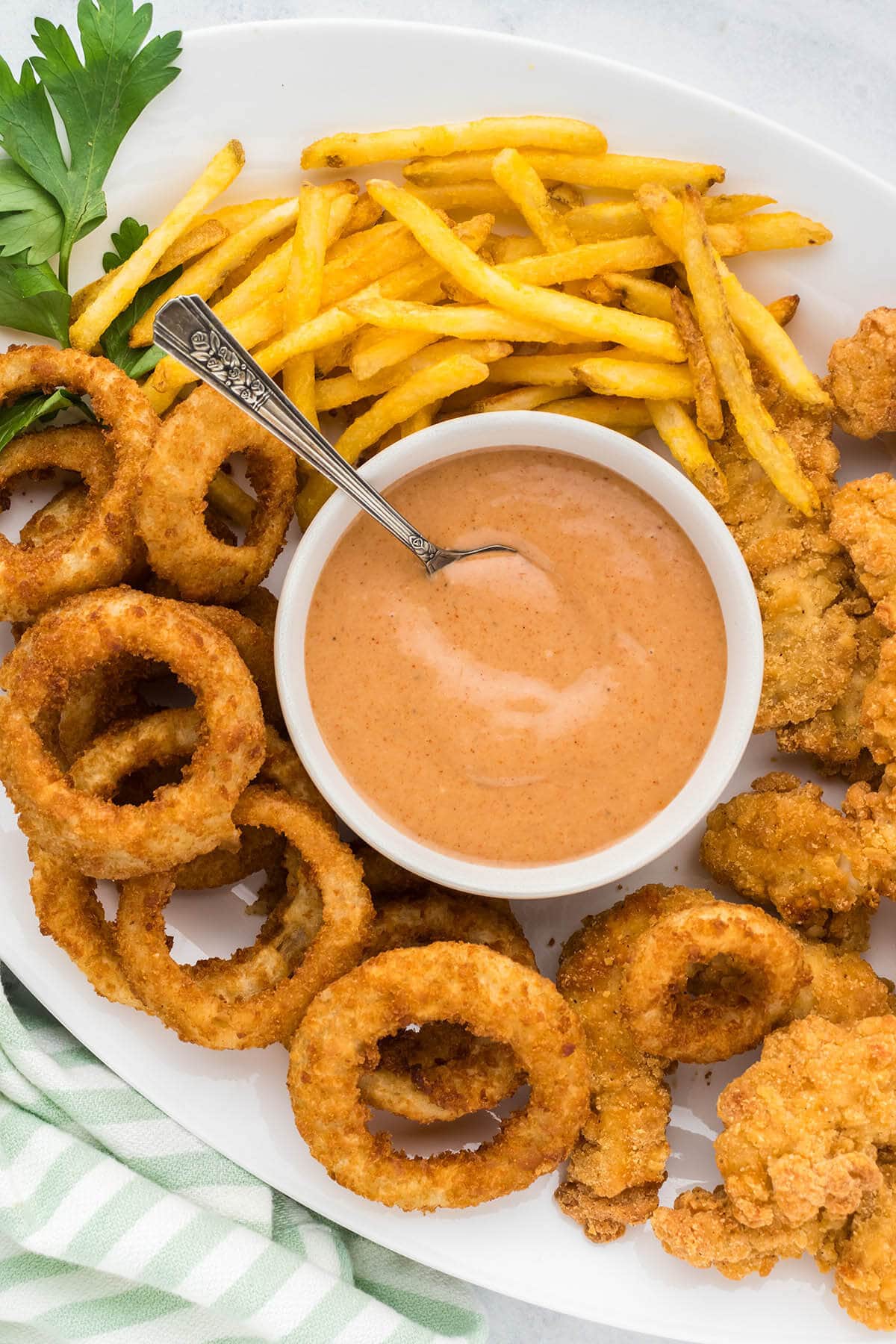 Red Robin Campfire Sauce in bowl with a serving spoon on a platter surrounded by fries, chicken strips and onion rings.