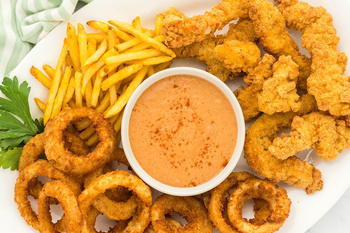 Red Robin Campfire Sauce in bowl on a platter surrounded by fries, chicken strips and onion rings.