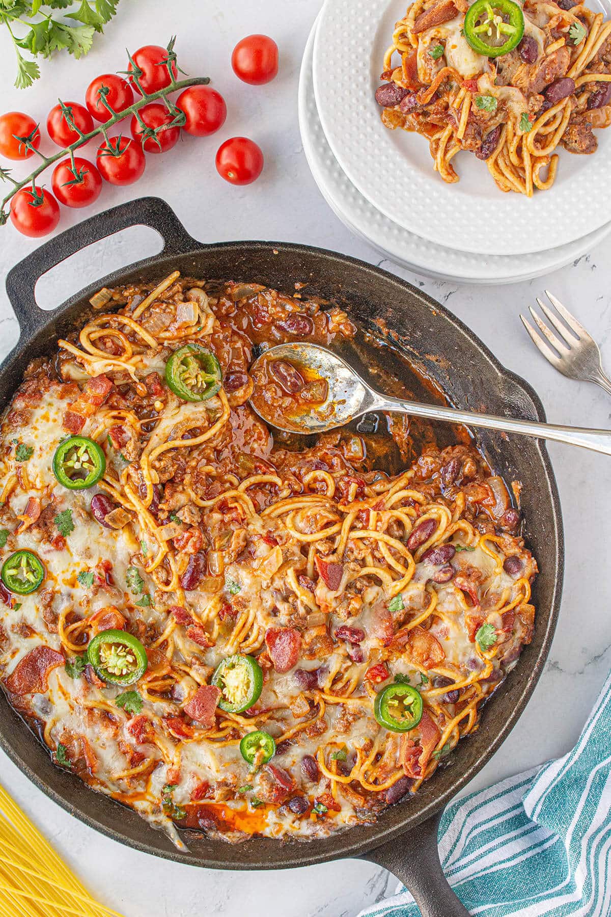 A cast iron skillet filled with chili spaghetti, with serving spoon.