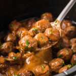 Saucy beef meatballs in crockpot with brown gravy. With serving spoon.