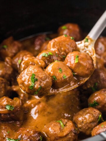 Saucy beef meatballs in crockpot with brown gravy. With serving spoon.