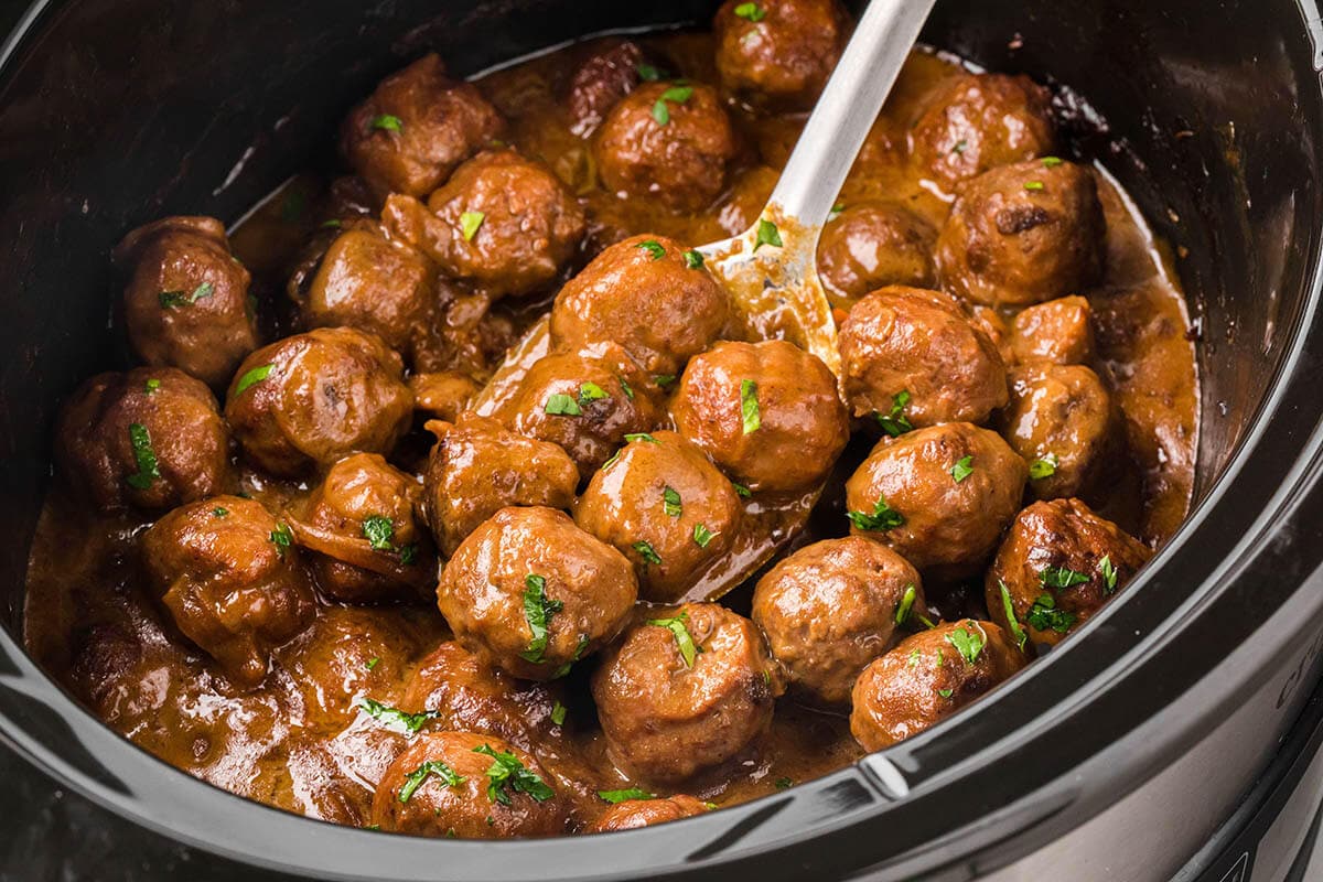 Crockpot filled with meatballs in a brown gravy. With a serving spoon.