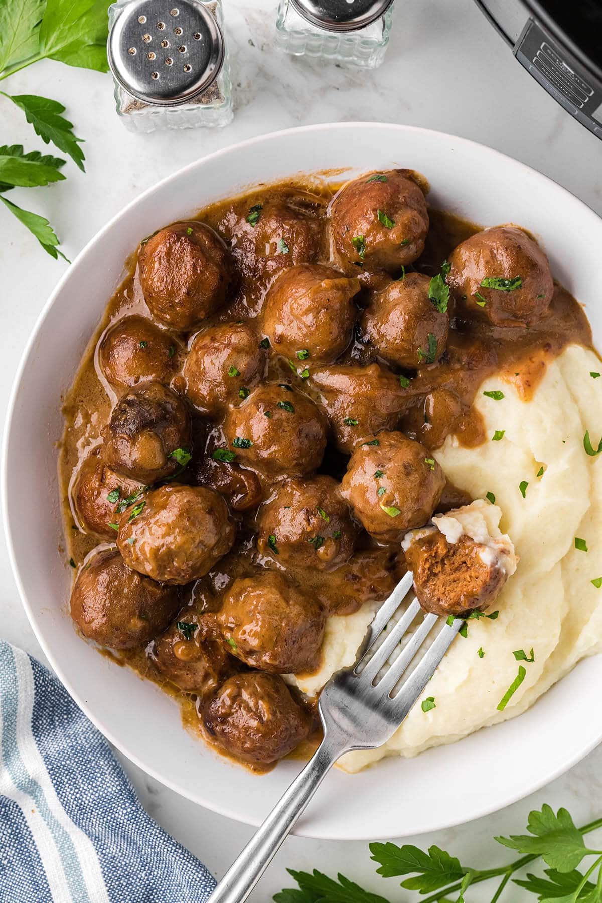 Saucy meatballs and gravy over mashed potatoes on a plate with a fork.