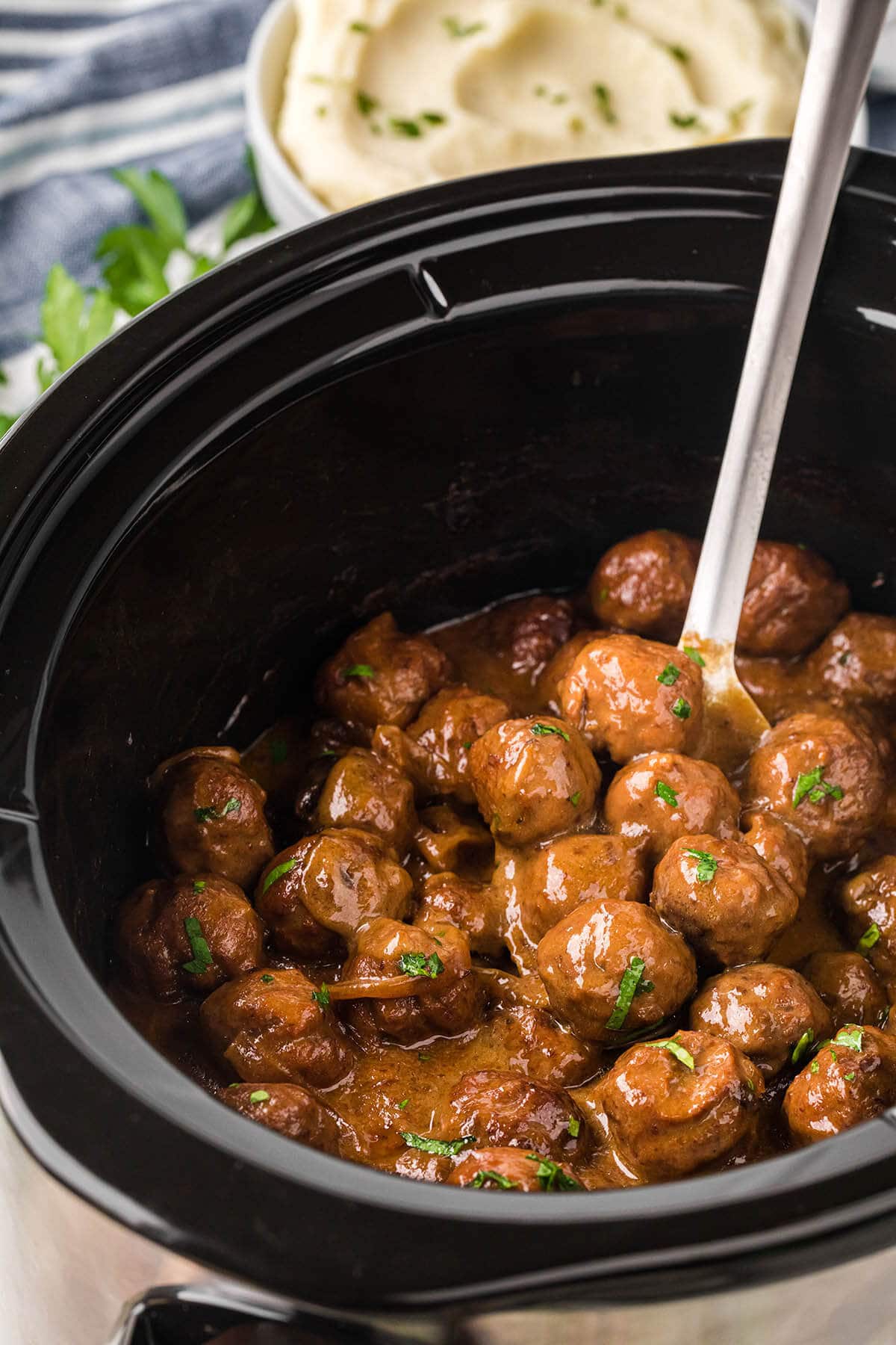 Slow Cooker with meatballs and gravy with serving spoon.