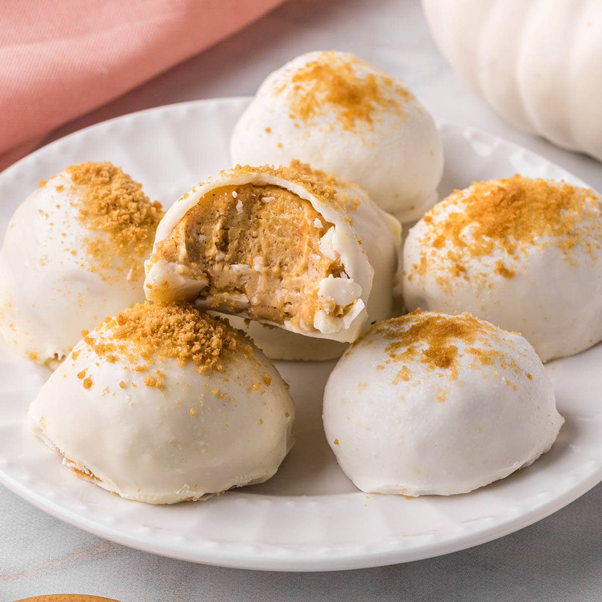 A platter filled with pumpkin truffles dipped in white chocolate and sprinkles with graham cracker crumbs.