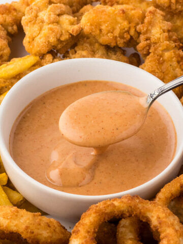 Red Robin Campfire Sauce in bowl with a serving spoon. It's surrounded by fries, chicken strips and onion rings.