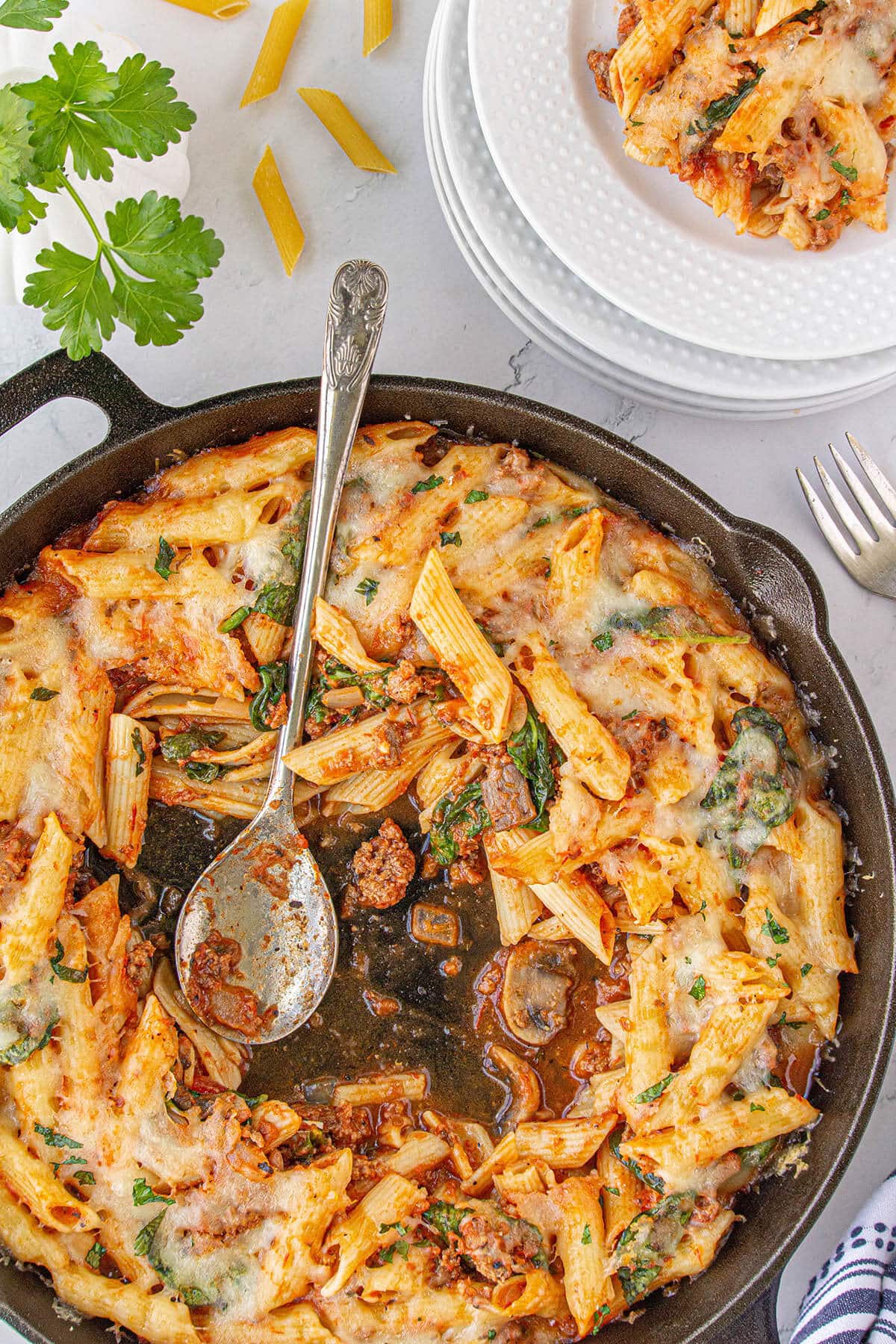 Cheesy Simple Sausage Pasta Bake in cast iron skillet with serving spoon.