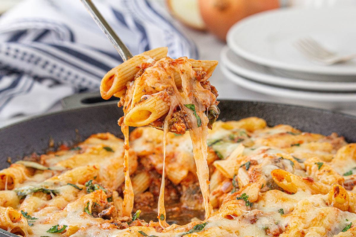 Cheesy pasta casserole with a spoon grabbing a big helping.
