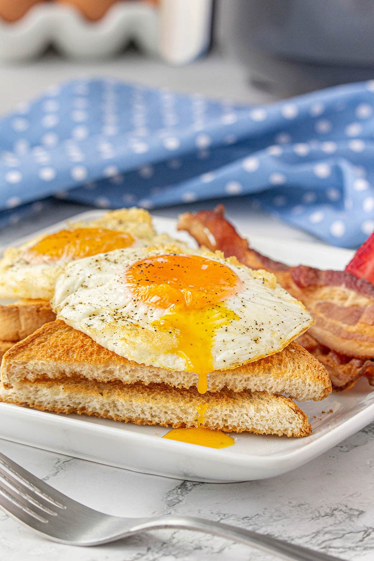 Fried eggs over toast on a plate with bacon.
