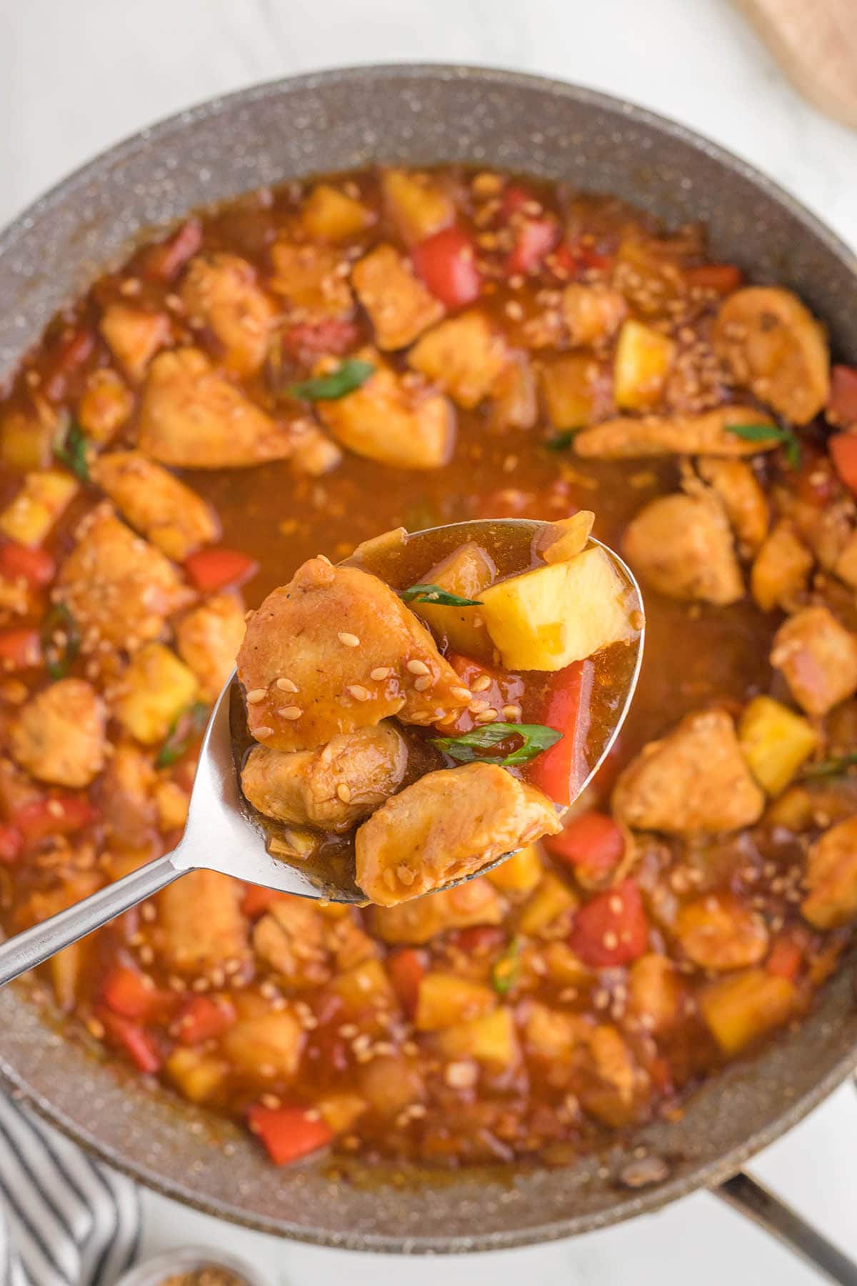 Overhead shot of pan filled with sweet and sour chicken. With a serving spoon.