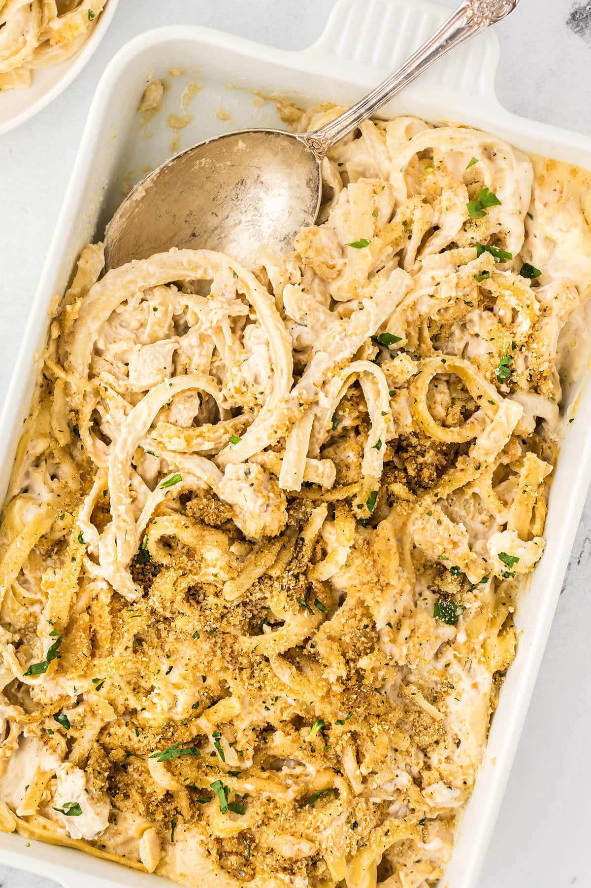 Chicken and Fettuccini Alfredo Pasta Bake in a casserole dish with a serving spoon.